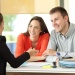 Person in business attire meeting with two clients across a desk during a consultation in a modern office.